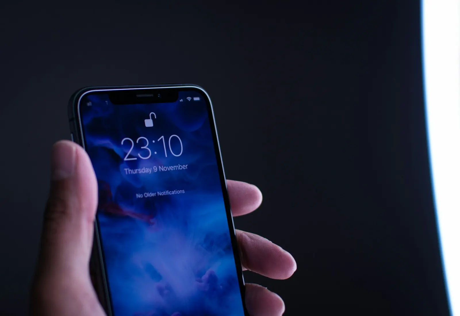Hand holding a smartphone with its lock screen lit in a dark room