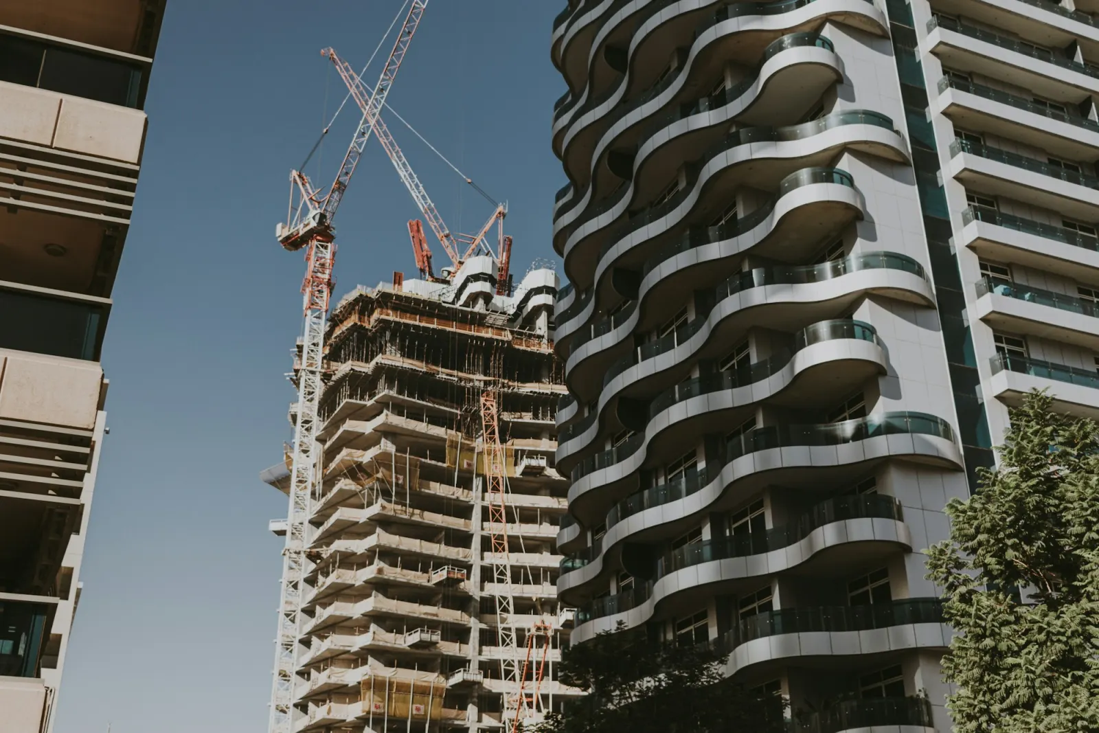 Residential tower under construction next to a completed tower with curved balconies
