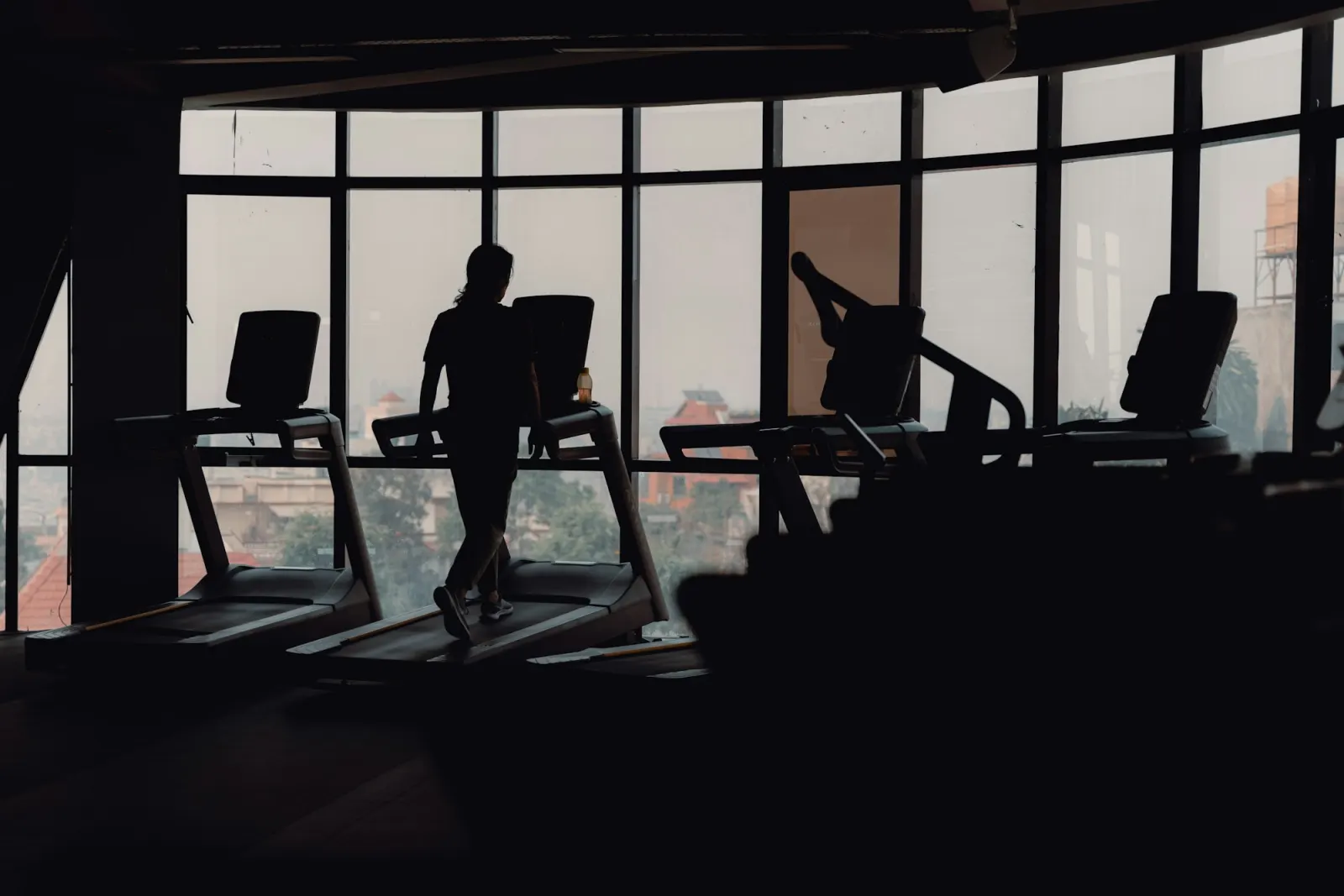Silhouettes of people running on treadmills by a large window
