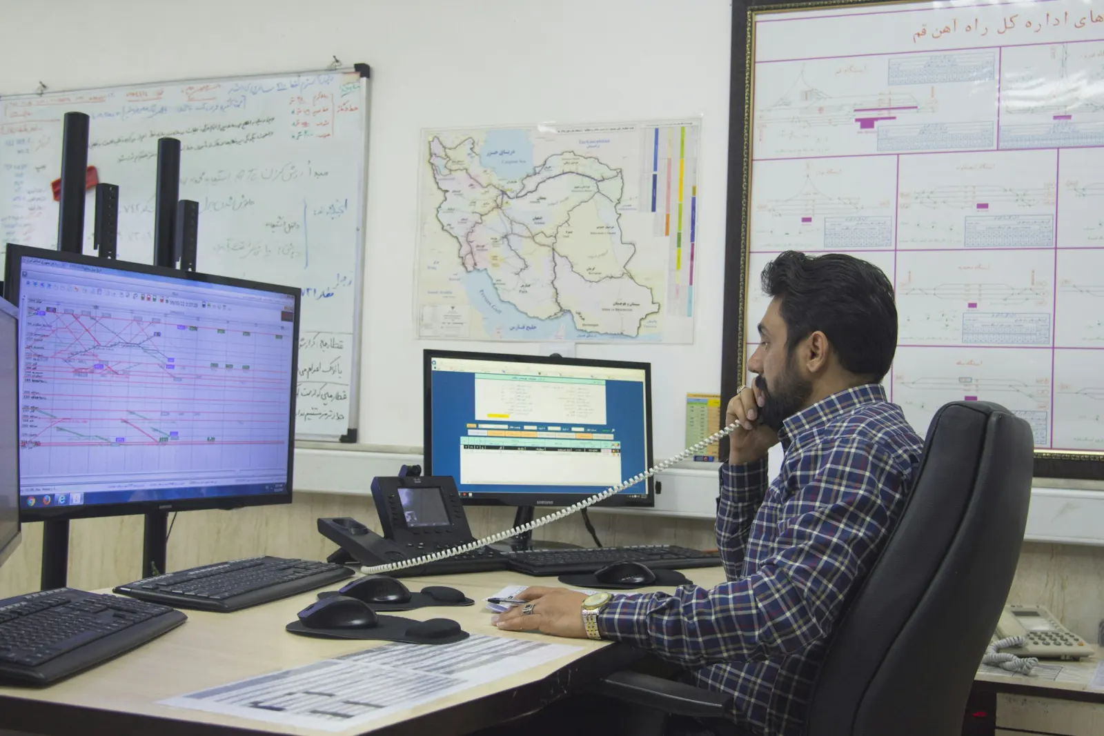 Logistics coordinator on the phone at a desk with monitors and a route map