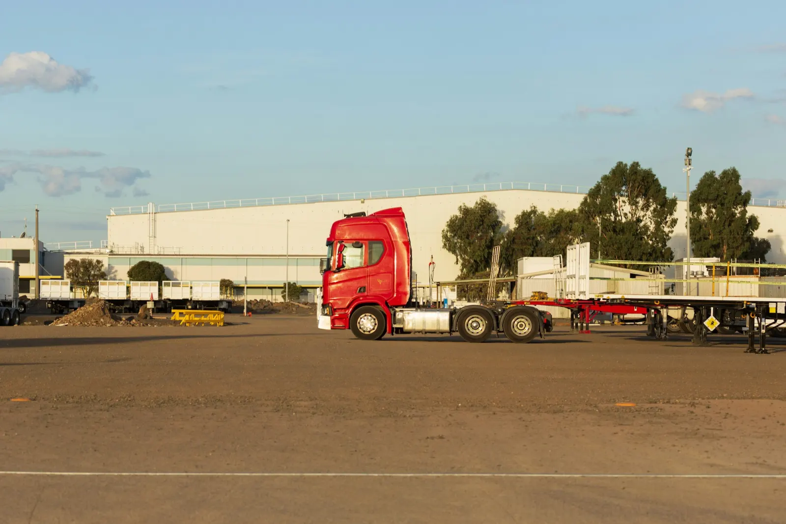 Red truck with a flatbed trailer parked at a logistics depot