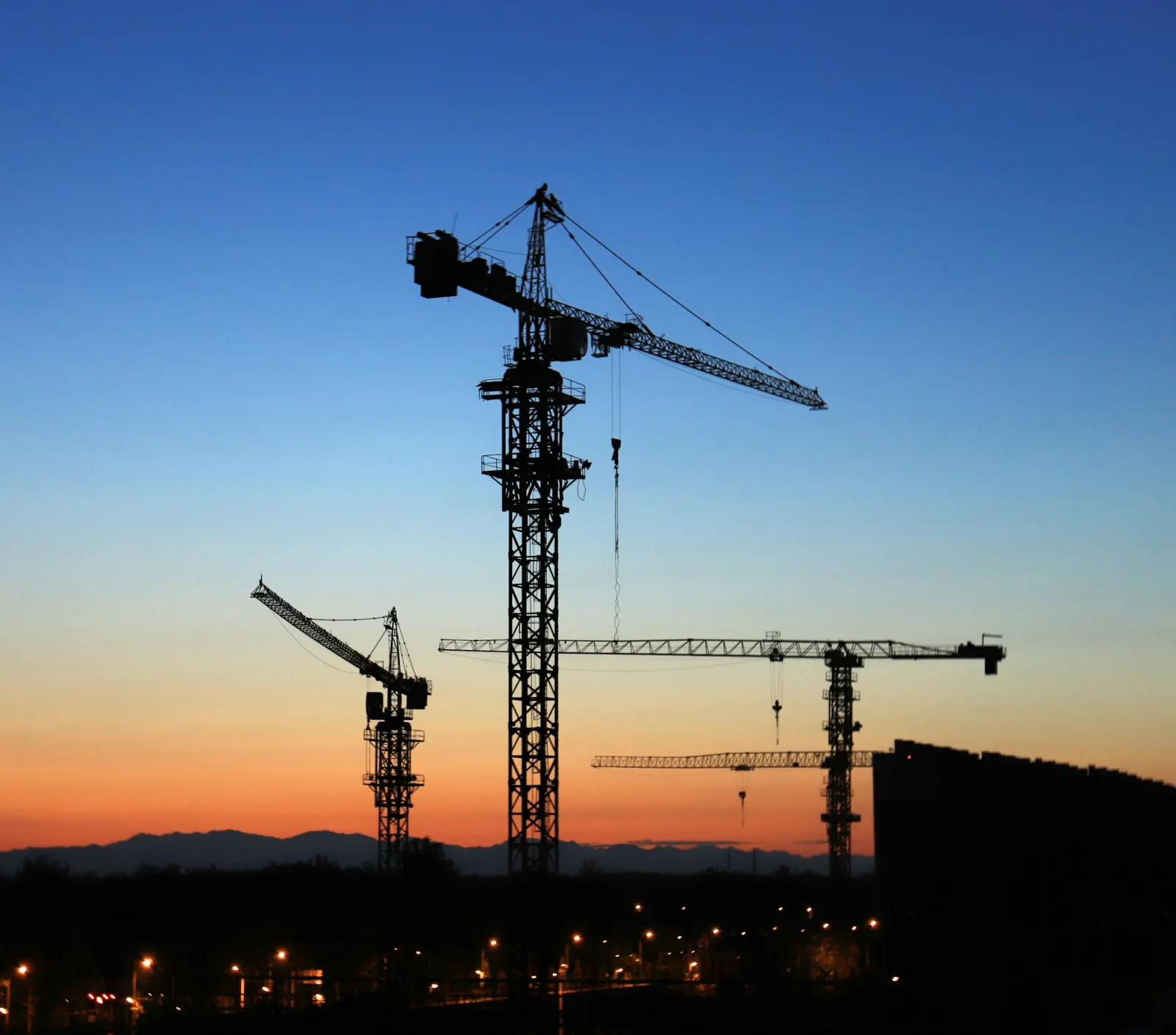 Tower cranes silhouetted against a sunset sky
